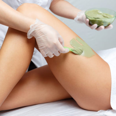 Cosmetologist applies seaweed mud on a  woman's hip in a cosmetological beauty clinic