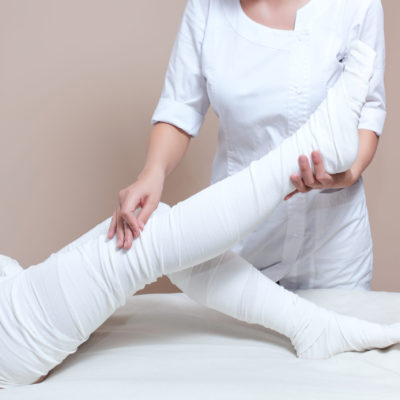 The cosmetologist wraps the leg of the customer. Anti-cellulite procedure-STYX wrap.